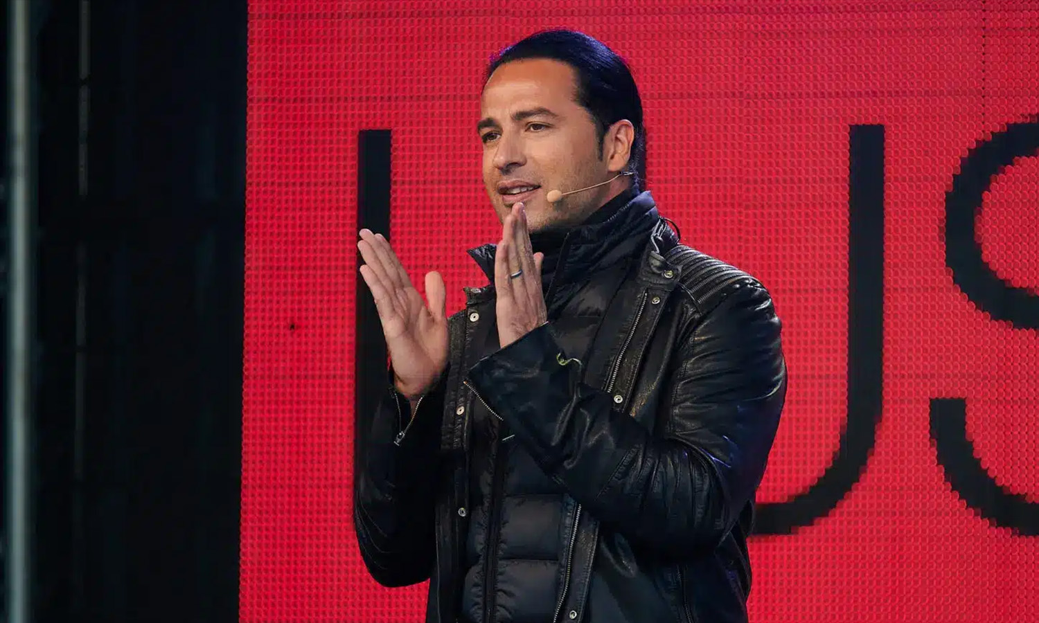 Comedian Bülent Ceylan performt energiegeladen auf der Bühne vor hunderten parkenden Autos in der CARantena Arena Worms.